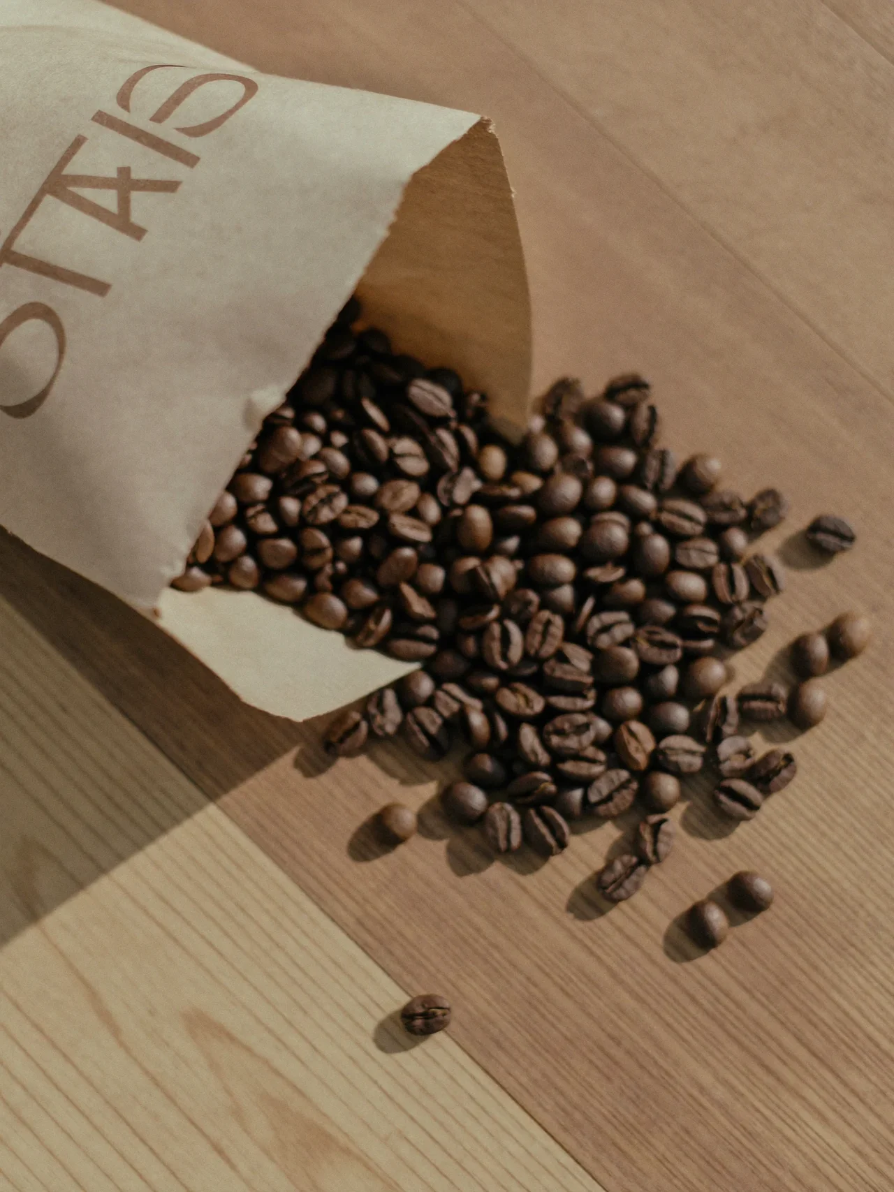 Frisch geröstete Kaffeebohnen in einer schlichten Papiertüte auf hellem Eichentisch